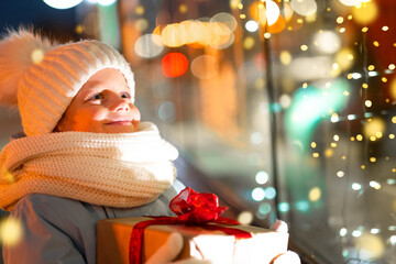 Portrait Boy with Gifts box looking and dreaming in Christmas window shopping on traditional...