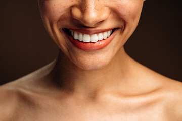 Cropped view of the multiracial woman smiling toothy and posing to the camera while standing in front of the brown wall. Stock photo