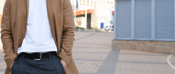 Cropped man in coat holding hands in pocket of pants on urban street, banner 