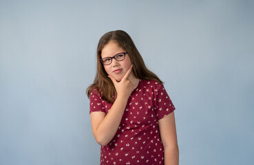 Thoughtful Young Girl with Glasses Posed with Fingers on Chin Blue Background with Copy Space