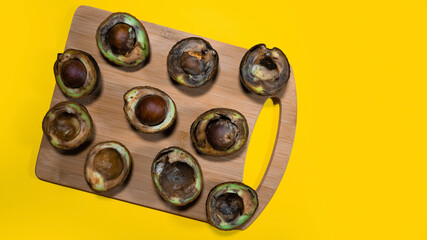 Overripe Avocado on wood Chipper on yellow background. Rotten Avocado Fruits in the kitchen on table. Unhelthy food concept. Stop wasting food. Copy space.