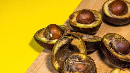 Bad Avocado Halfs on Yellow background. Bad Vegan food. Rotten Avocado on wood Chipper next fork and knife. Necomestibile Food. Stop wasting food. Overripe Fruits Concept cannot be eaten. Copy space.