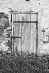 Stare drewniane drzwi z metalowymi zardzewiałymi okuciami w ścianie z cegły. Odpadający tynk ze...
