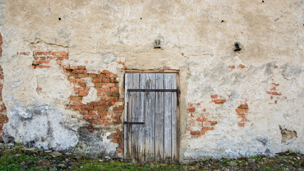 Stare drewniane drzwi z metalowymi zardzewiałymi okuciami w ścianie z cegły. Odpadający tynk ze ściany.