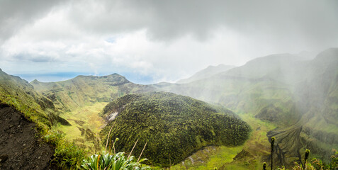 La Soufriere volcano crater panorama with tuff cone hidden in green and pouring rain, Saint Vincent...