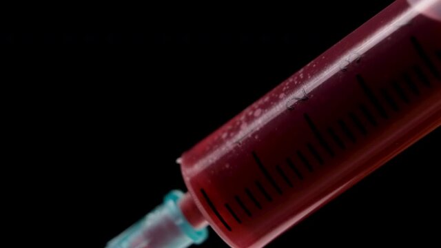 Extreme close-up, drawing blood sample with a medical syringe isolated on black background. Syringe being filled with red liquid. Macro shot medical procedure. 4k resolution.