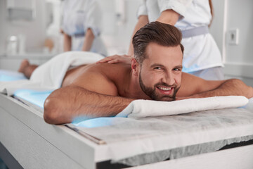 Happy mature man undergoes massage procedure with professional chiropractics in clinic