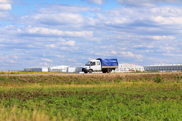 a truck with a blue awning drives along the highway past a farm in summer on a sunny day