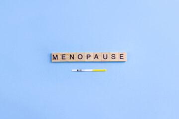 Word menopause on wooden blocks with letters and rapid FSH test. Minimal concept of female periods. Copy space