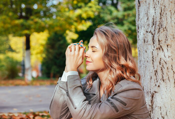 Portrait of a young dreamy woman in an autumn park. A young girl sits in the rays of sunlight with closed eyes under a tree in an autumn park.