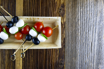 Top view and close up of aperitif snacks of tomatoes, olives, mozzarella and basil on wooden background