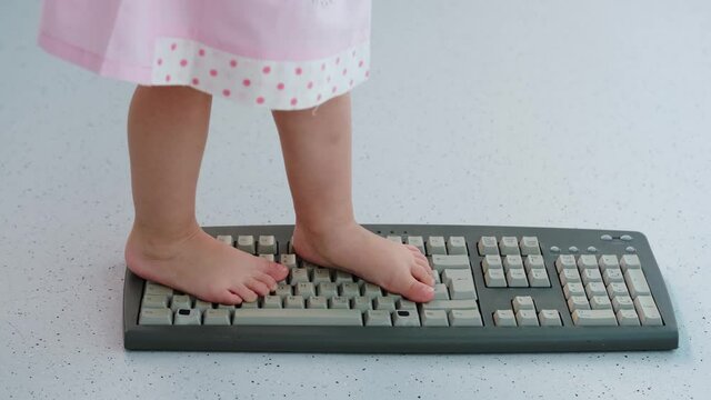 child stands, jumps, dances with his feet on computer keyboard, presses buttons, little vandal, bully plays with gadget, bullying concept, spoils technology until parents can see