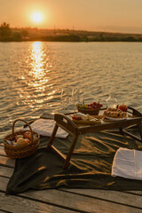 Amazing sunset on the lake, white wine, fruit cake, apples, grapes, brie cheese, biscuits. Autumn aesthetic picnic.