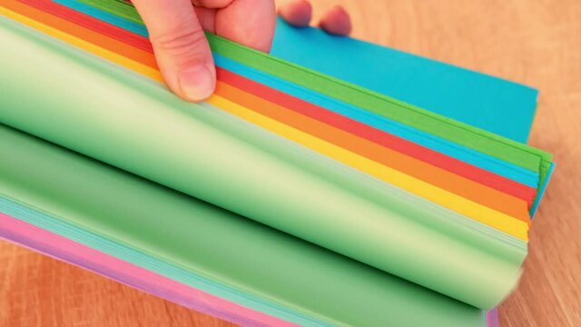 closeup woman holding a thick pile of colored paper for office, scrapbooking, origami, flips through blue, red, green, yellow sheets, concept of needlework, artisans crafting and creating by hand