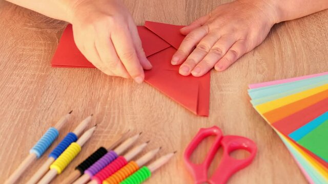 closeup woman holding colored paper, material for scrapbooking, origami, folds figures from paper, envelope in Japanese origami technique, concept of creating by hand for children's game
