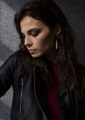 Profile portrait of a young woman in a black leather jacket and burgundy top standing in front of a sunlit window.