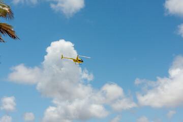Helicóptero voando com ceu azul e nuvens esparsas. 