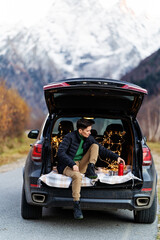 A woman sits in the trunk of a car against the background of mountains.