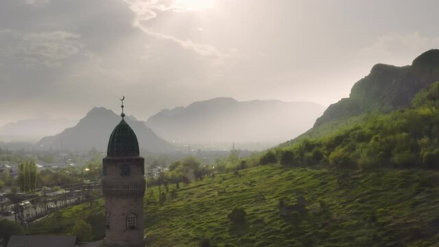 An aerial flight between the domes of the mosque against the background of the city, a misty green valley and large mountains in the rays of the contour sun. A beautiful landscape with stunning nature