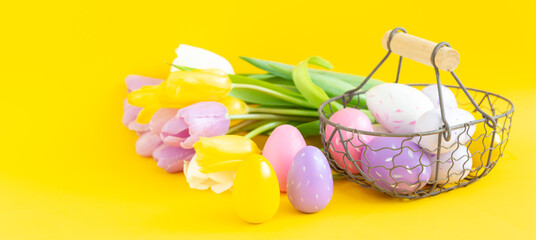 Easter composition. Multicolored easter eggs and tulips on yellow background. Easter concept. Copy space. Horizontal banner