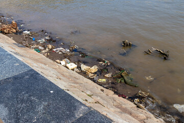 Garbage in the river along the city embankment. Ecological problem of pollution of reservoirs with...