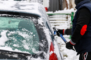 A man brushes snow from a car in the yard after a night snowfall