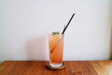 There is a glass of gradient-colored drink with a straw inserted on the white wall and wooden tabletop, a dreamy drink