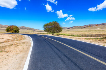 Asphalt highway and mountain scenery under blue sky.
