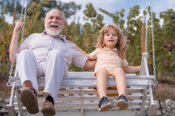Excited amazed young grandson and old grandfather swinging in spring garden. Grand dad and grandson...