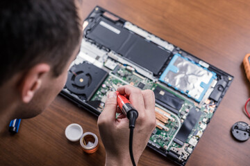 An engineer repairs a laptop and motherboard with a soldering iron, top view. Service center.