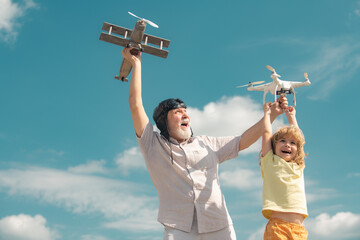 Grandson child and grandfather playing with toy plane and quadcopter drone against sky. Child pilot...