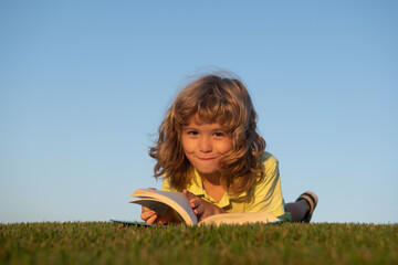 Kids imagination, dreaming children. Cute kid reading book on green grass.