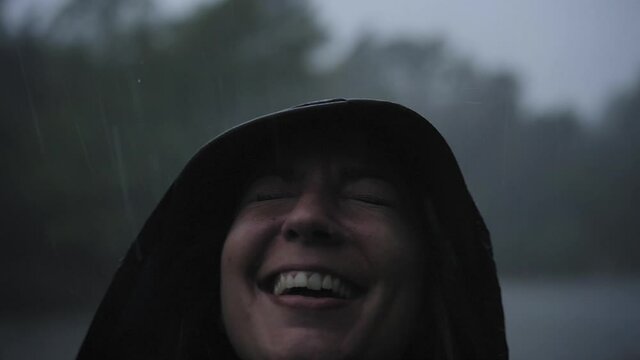 Smiling woman in the rain enjoying the nature wearing raincoat. The drops fall on his face and the girl is happy. Concept of nature, freedom, purity...