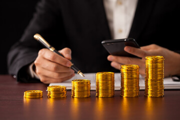 a man calculating on desk with stacks of rising gold coins.  