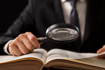 a man's hand holding a magnifying glass looking for information on book.