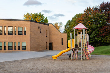 School building and schoolyard with playground without children in Canada.