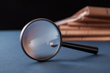 close up magnifying glass in front of stack files on blue table.