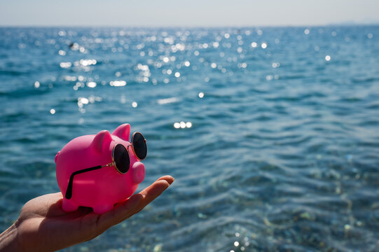 A woman holds a piggy bank in sunglasses on the background of the sea. Budget vacation.