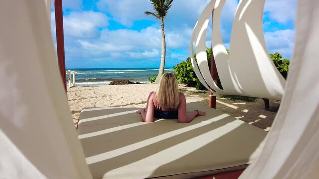Blonde Woman in Bathing Suit Lounging in a Beach Cabana in the White Sand and Blue Water at a Tropical Resort (4k) 