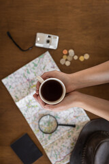 Flat lay, map, magnifier, documents and a cup of coffee in the hands of a woman.