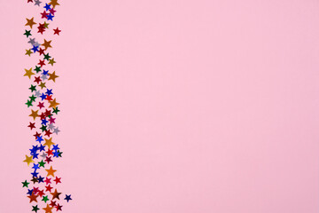 Pink background,a strip on the side with a brilliant sparkling glitter in the form of multicolored stars of different sizes.A festive concept.Christmas, birthday and other celebrations.Place for text