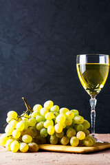 a brush of white grapes on a cutting board in the background a glass of white wine on a black background