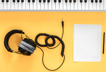 Headphones, musical keys and a blank sheet of paper on a yellow background.