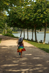 Scener of the lake with a little girl in rainbow dress running on the concrete path in the park.