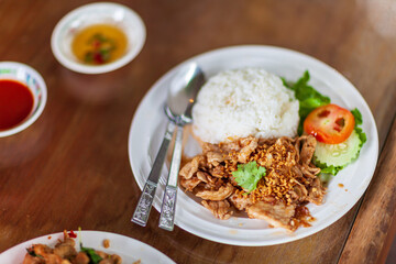 pork stir-fried with garlic rice in white plate on the table set, a popular meal in Thailand.selective focus.