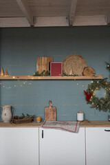 Obraz na płótnie Canvas Minimalist home interior with cozy kitchen furniture, kitchenware, Christmas wreath on dusty blue wall. Scandinavian hygge style Christmas decor