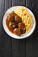 Boulets liegeois is a popular dish served all over Belgium made of meatballs swimming in an apple and onion gravy served with fries closeup in the plate on the table. Vertical top view from above