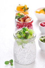 Chia pudding assortment with fruits and yogurt served in glass jars on the white table. Set of three healthy breakfast variations with kiwi, mango and figs