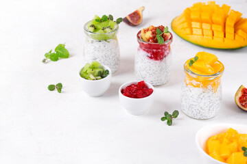 Chia pudding assortment with fruits and yogurt served in glass jars on the white table. Set of three healthy breakfast variations with kiwi, mango and figs