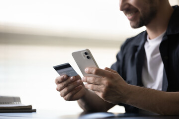 Close up happy young man holding credit card and smartphone in hands, purchasing goods or service in internet store, shopping in mobile app, satisfied with successful financial operation or security.